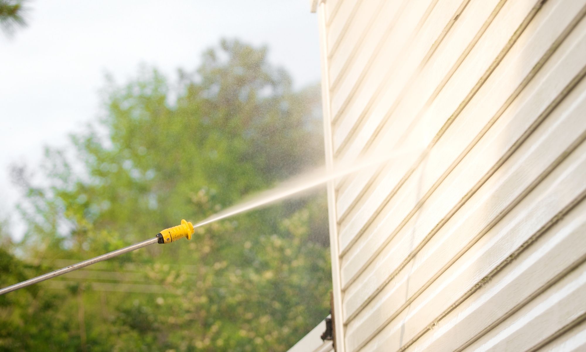 A person uses a pressure washer for house washing, spraying high-pressure water to clean the exterior siding.