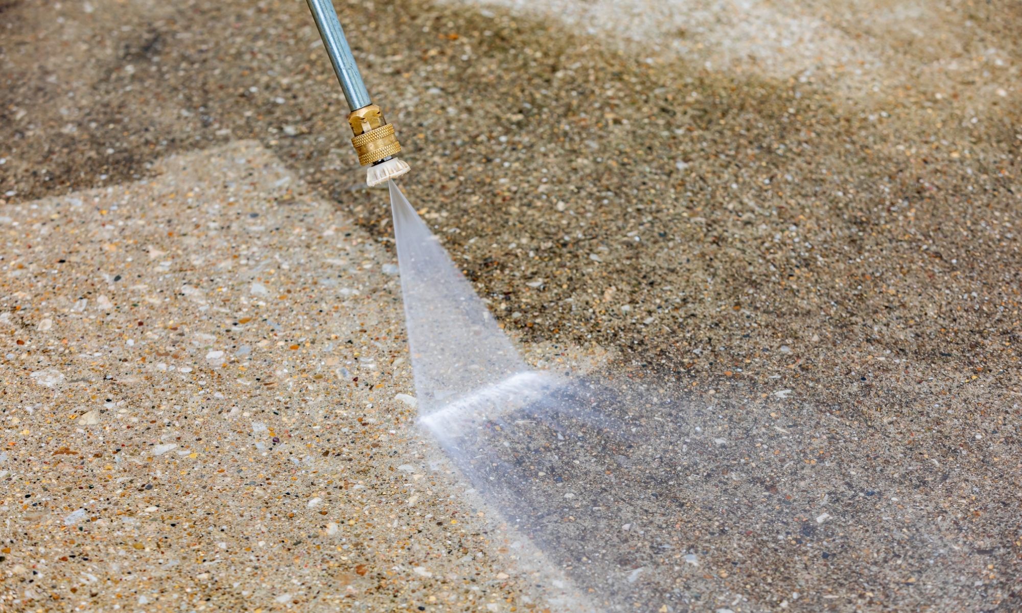 Pressure washer nozzle spraying water across a speckled concrete surface.