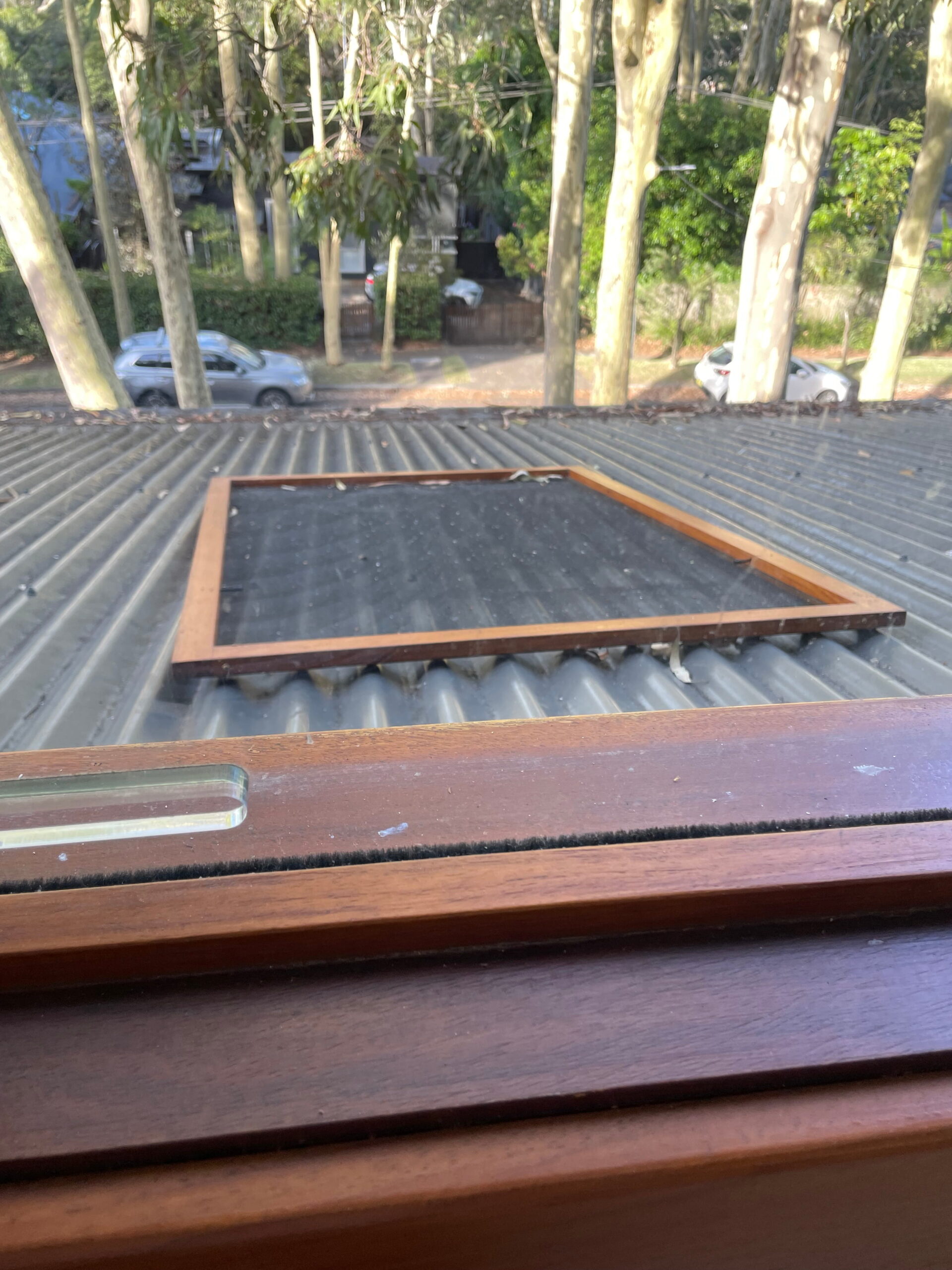 Property inspection window view shows a corrugated metal roof, rectangular wooden frame, trees, and parked cars outside.