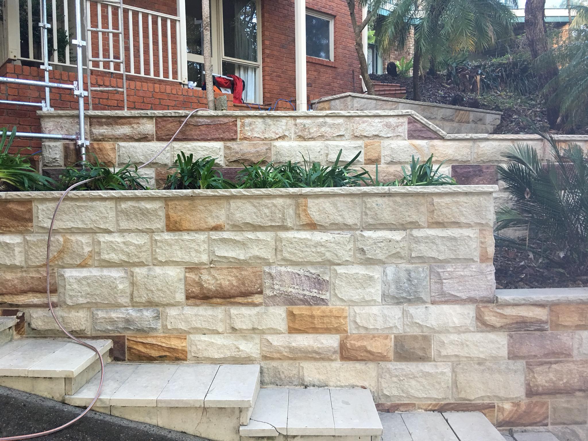 Stone retaining walls, garden beds, steps, and white railing in front of a brick house after expert pressure cleaning.