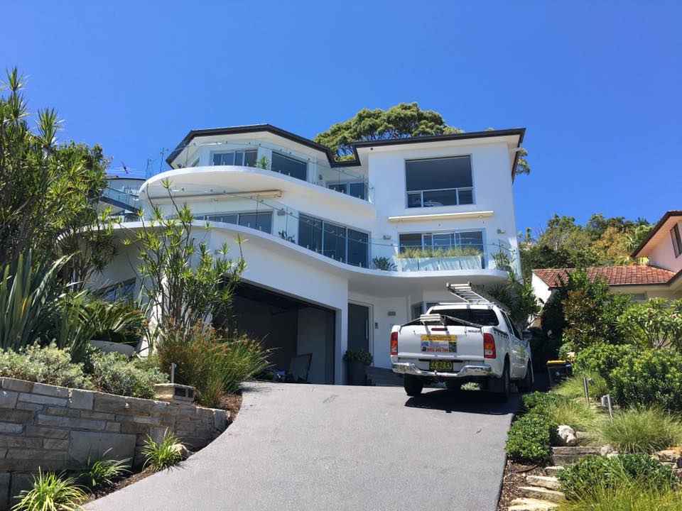 White modern three-story house with balconies, open garage, white pickup truck after house washing, greenery, blue sky.