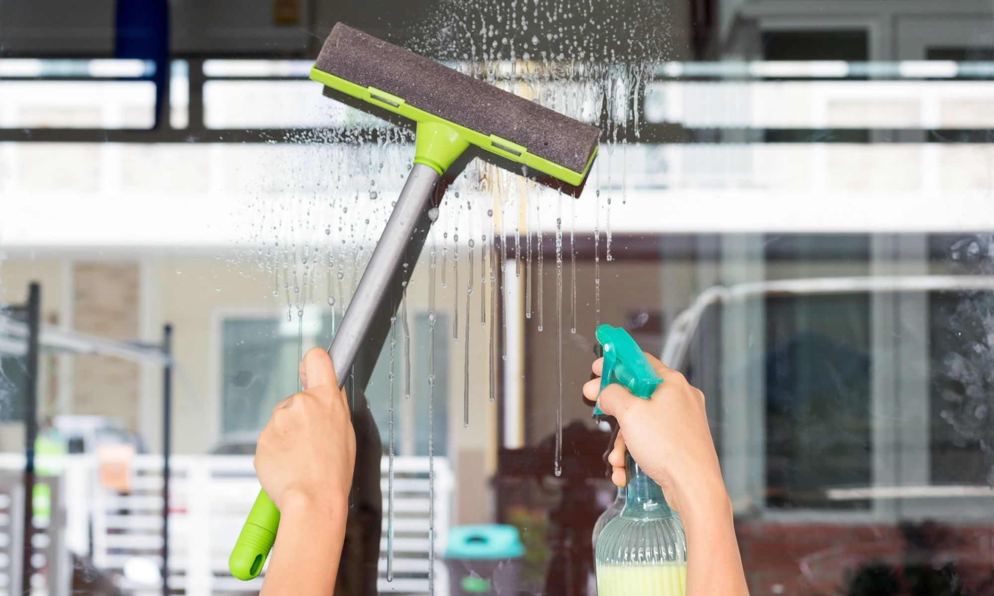 Person cleaning a window with squeegee and spray bottle for a sparkling view, highlighting window cleaning tools.